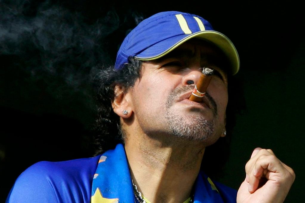 FILE - In this March 26, 2006 file photo, former soccer player Diego Maradona smokes a cigar as he watches Argentina's first division soccer match between Boca Juniors and River Plate  in Buenos Aires, Argentina. The Argentine soccer great who was among the best players ever and who led his country to the 1986 World Cup title before later struggling with cocaine use and obesity, died from a heart attack on Wednesday, Nov. 25, 2020, at his home in Buenos Aires. He was 60. (AP Photo/Natacha Pisarenko, File)