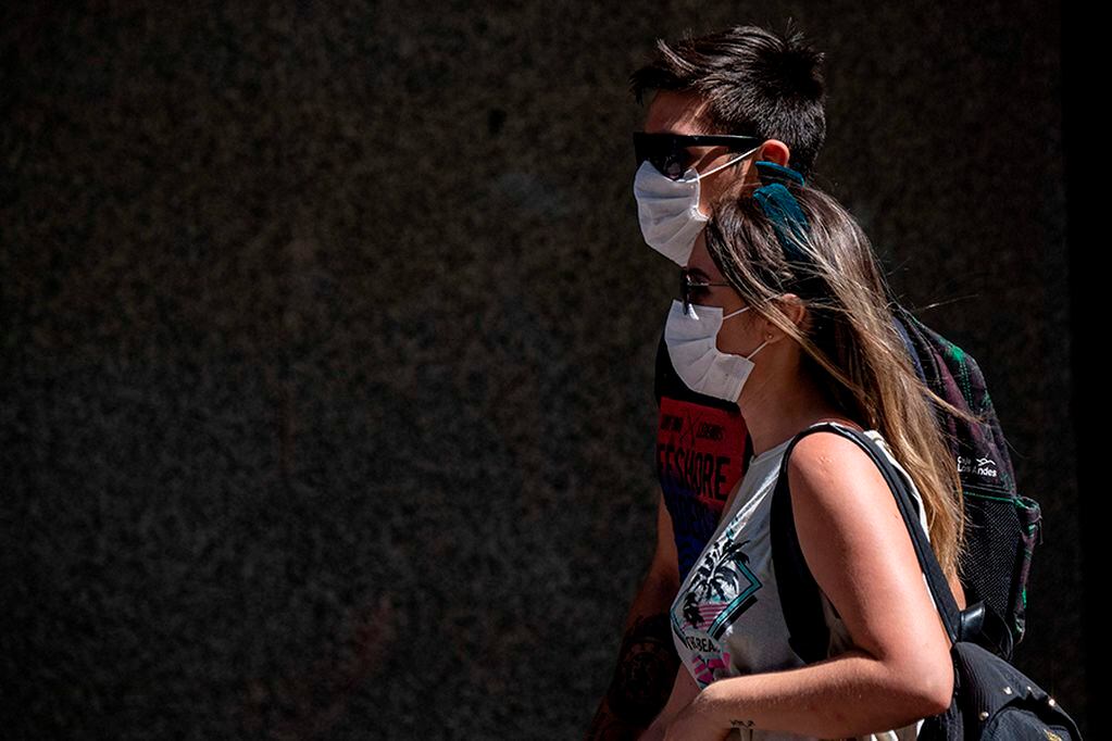 Pedestrians wear face masks as a precautionary measure against the spread of the new coronavirus, COVID-19, as they walk near La Moneda Presidential Palace in Santiago, on March 16, 2020. - Chile announced the closure of all borders after the number of people infected with coronavirus in the country duplicated in the last 24 hours, from 75 to 155, President Sebastian Pinera reported on Monday. (Photo by Martin BERNETTI / AFP)