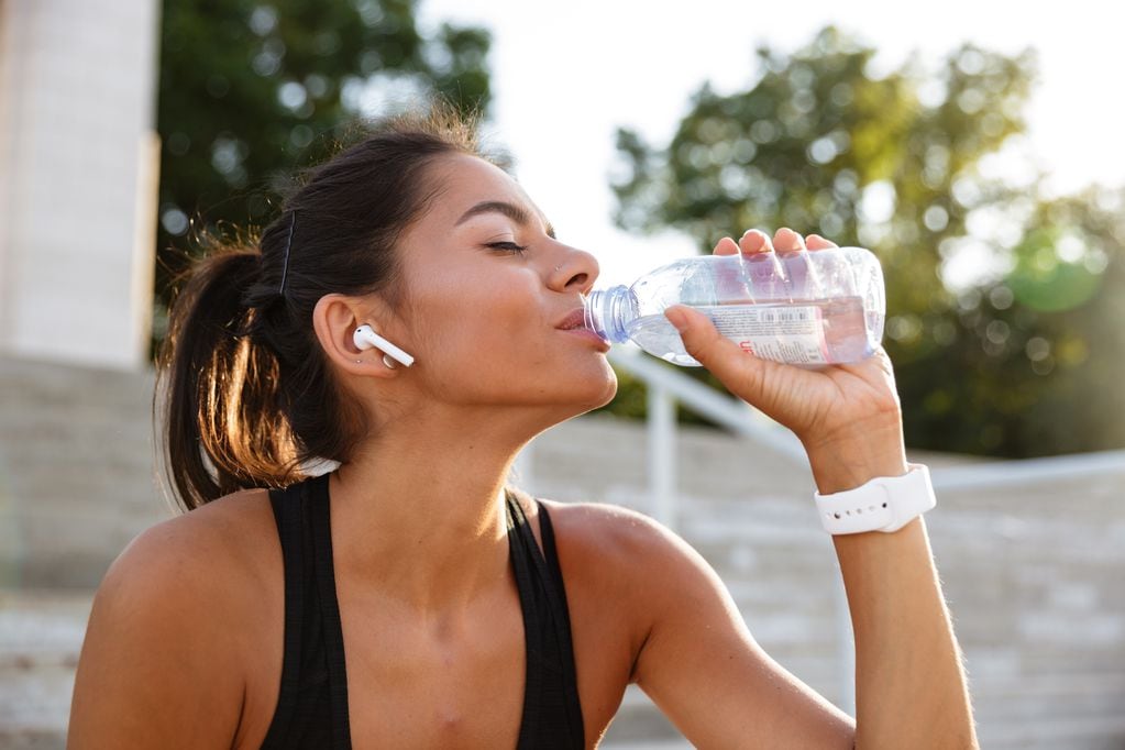 Portrait of a young fitness girl in earphones sitting on stairs outdoors and drinking water