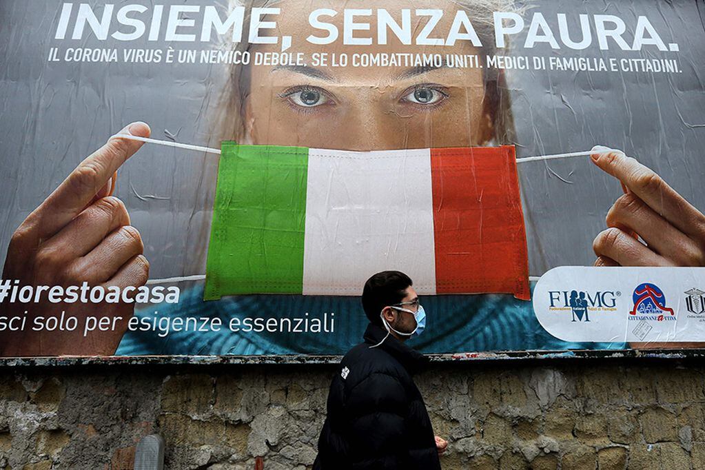 A man walks past a large billboard raising awareness to the measures   taken by the Italian government to fight against the spread of the COVID-19 (novel coronavirus) which pictures a woman wearing Italy's national flag as a facemask for protective measures and reads "All together, without fear", in the streets of Naples on March 22, 2020. - Italian Prime Minister, on March 21, ordered all non-essential companies and factories to close nationwide to stem a coronavirus pandemic that has killed 4,825 people in the country in a month. (Photo by Carlo Hermann / AFP)