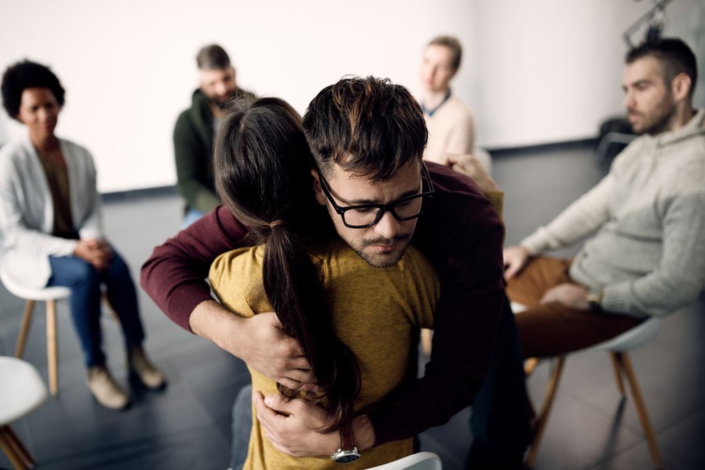 Young man embracing female member of group therapy during a session at community center.