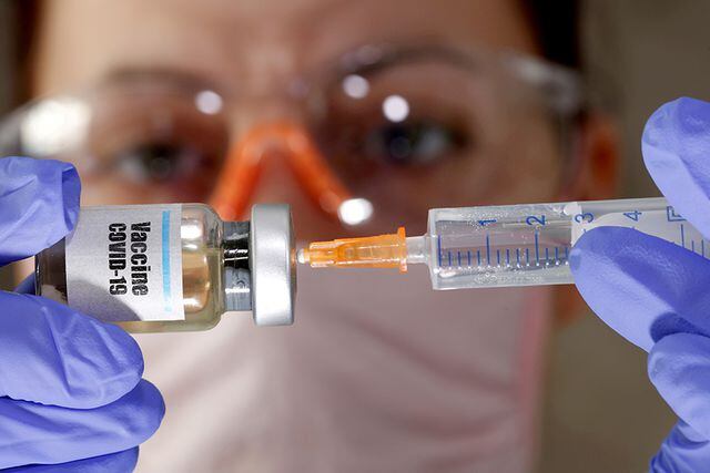 FILE PHOTO: FILE PHOTO: A woman holds a small bottle labeled with a "Vaccine COVID-19" sticker and a medical syringe in this illustration