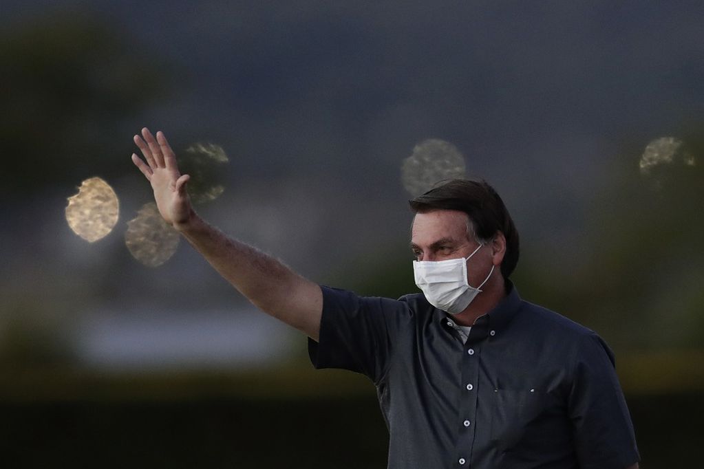Brazil's President Jair Bolsonaro who is infected with COVID-19, wears a protective face mask as he waves to supporters during a Brazilian flag retreat ceremony outside his official residence the Alvorada Palace, in Brasilia, Brazil, Monday, July 20, 2020. (AP Photo/Eraldo Peres)