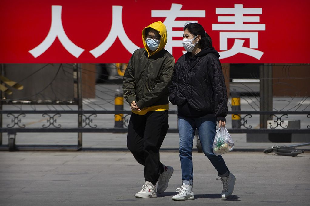 People wearing face masks to protect against the spread of the new coronavirus walk in front of a propaganda billboard reading "it is everyone's responsibility to control the spread of disease" at a public park in Beijing, Tuesday, April 21, 2020. China reported about a dozen coronavirus cases Tuesday, about half of them in the province of Heilongjiang that borders Russia. (AP Photo/Mark Schiefelbein)