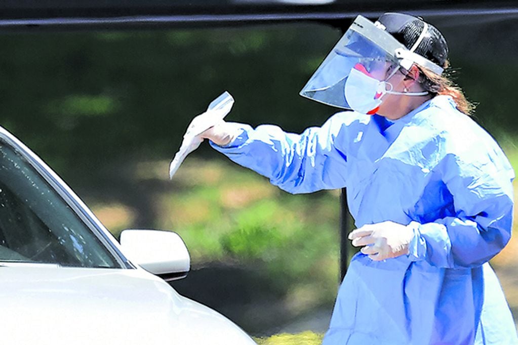 A healthcare volunteer in protective gear delivers a novel coronavirus, COVID-19, test kit to a driver at a mobile test site in Los Angeles, Caifornia on May 6, 2020. - Some retailers in California, including bookstores, flower shops and clothing stores, will be allowed to reopen for business at the end of the week, the state's governor announced on Monday. (Photo by Frederic J. BROWN / AFP)