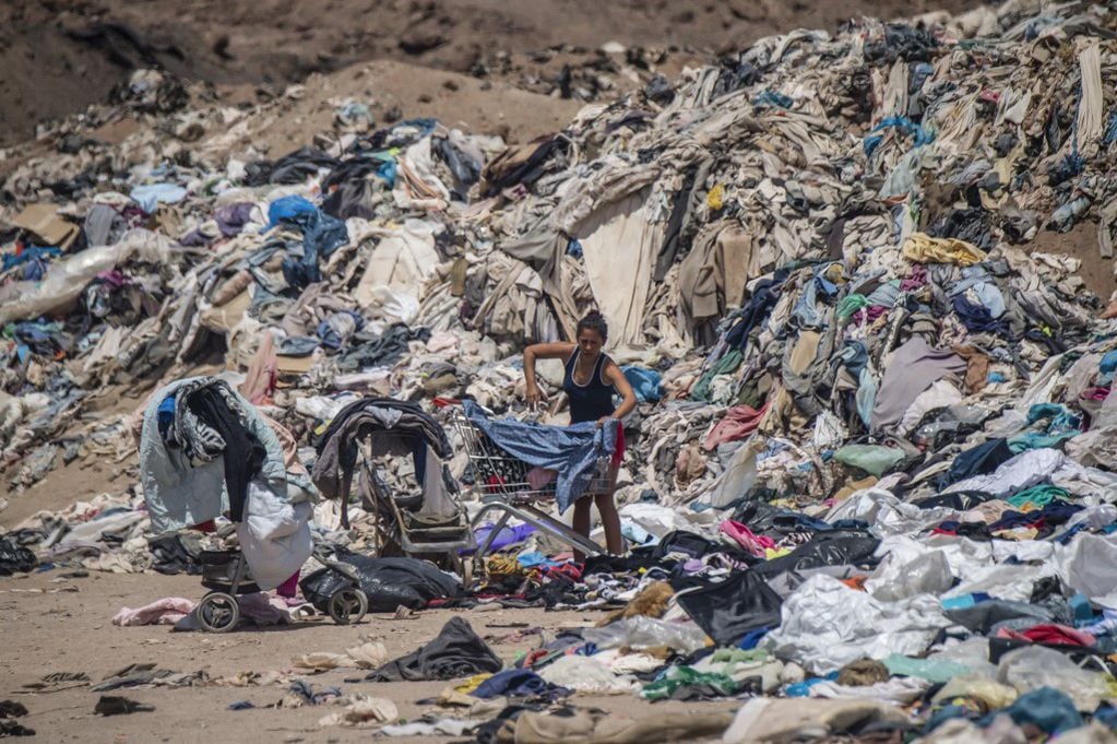 (FILES) In this file photo taken on September 26, 2021, a woman searches for used clothes amid tons discarded in the Atacama desert, in Alto Hospicio, Iquique, Chile. - The Chilean justice system is investigating the huge used clothing dump located in the Atacama desert, for environmental damage, the First Environmental Tribunal reported on August 3, 2022. The tons of textile waste and other items such as tyres, car parts and electronics, that have been dumped in the Alto Hospicio area can now be seen partially burned and buried. (Photo by Martin BERNETTI / AFP)
