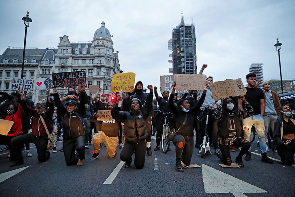 Protestors hold placards as they kneel in front of Police vans in Parliament Square, during an anti-racism demonstration in London, on June 3, 2020, after George Floyd, an unarmed black man died after a police officer knelt on his neck during an arrest in Minneapolis, USA. - Thousands of people took to the streets of London on Wednesday to protest the death of George Floyd in US police custody, as Prime Minister Boris Johnson condemned the killing and told President Donald Trump that racist violence had "no place" in society. Protesters, many of them in face masks, defied coronavirus restrictions and held aloft signs saying "Justice for George Floyd" and "Enough is enough!" as they marched from Hyde Park to the Whitehall government district in central London. (Photo by Tolga AKMEN / AFP)