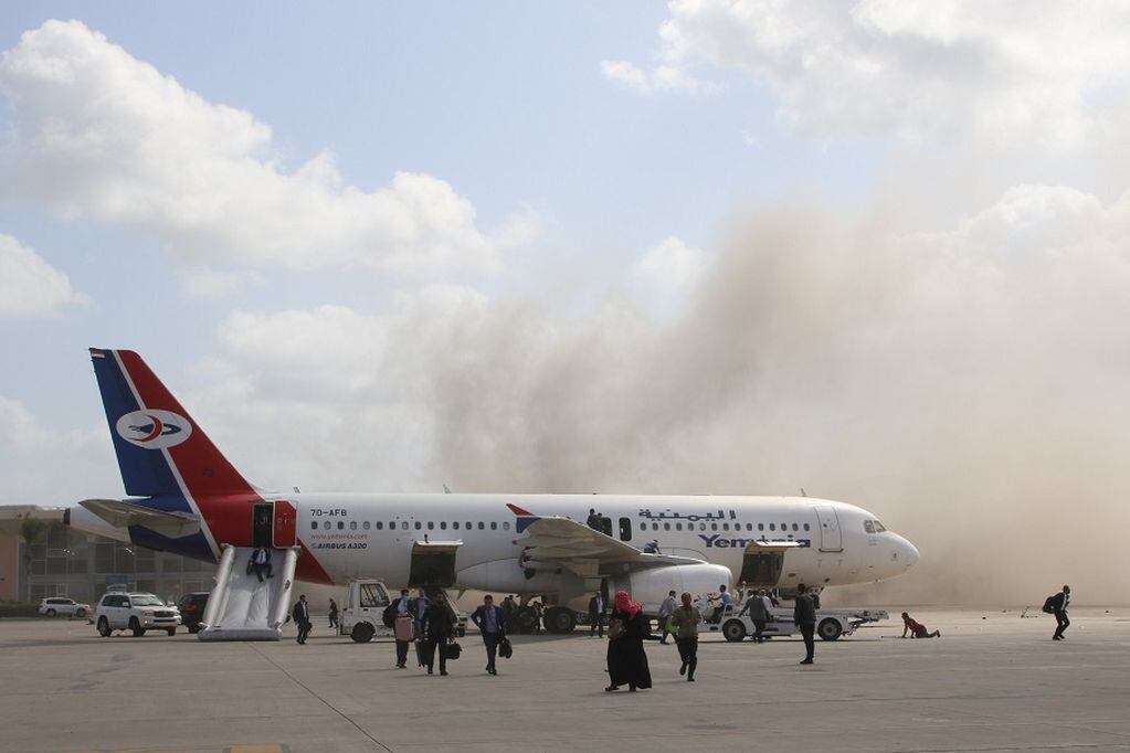 People walk on the tarmac as dust and smoke rise after explosions hit Aden airport, upon the arrival of the newly-formed Yemeni government in Aden, Yemen December 30, 2020. REUTERS/Fawaz Salman