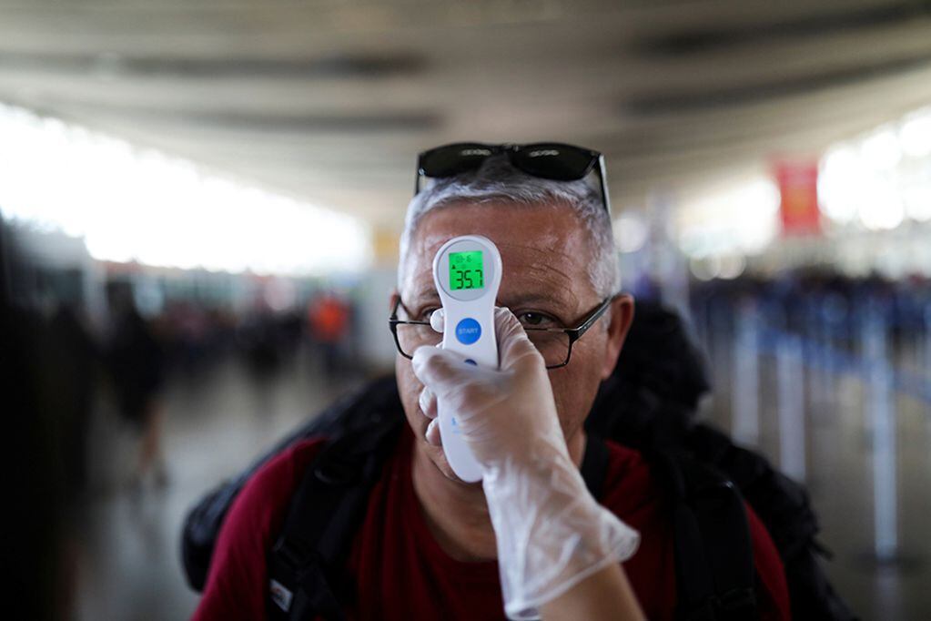 An employee takes the temperature of a man as a preventive measure against the coronavirus disease (COVID-19) in the Santiago's International airport, in Santiago, Chile March 16, 2020. REUTERS/Pablo Sanhueza