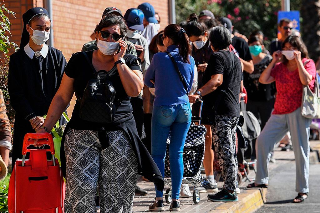 People queue to shop at a supermarket in Santiago, Chile, on March 26, 2020. - More than 1.3 million people of seven of the main communes of Santiago will enter into total quarantine for a week starting Thursday night, after prolonging the suspension of classes due to the coronavirus epidemic that has left 1,306 confirmed cases and four deceased. (Photo by MARTIN BERNETTI / AFP)