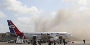 People walk on the tarmac as dust and smoke rise after explosions hit Aden airport, upon the arrival of the newly-formed Yemeni government in Aden