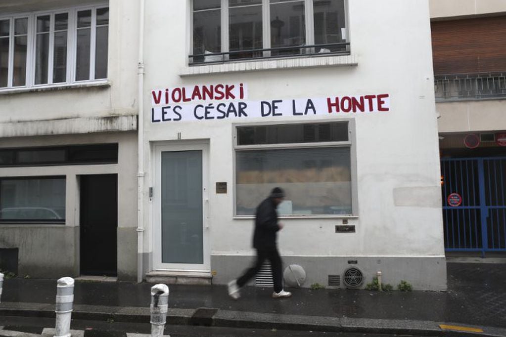 A man walks by the Academie des Cesar headquarters where a graffiti reads "Violanski, Cesar awards of shame", playing with the French word for rape and the name of Roman Polanski, Thursday, Feb. 27, 2020 in Paris. French women's rights activists are plastering banners to protest multiple nominations for Roman Polanski at the Cesar Awards ceremony, France's equivalent of the Oscars. This year's Cesars have been shaken by boycott calls since the nominations for Polanski's "An Officer and a Spy," because a French woman recently accused Polanski of raping her in the 1970s, which he denies. (AP Photo/Thibault Camus)
