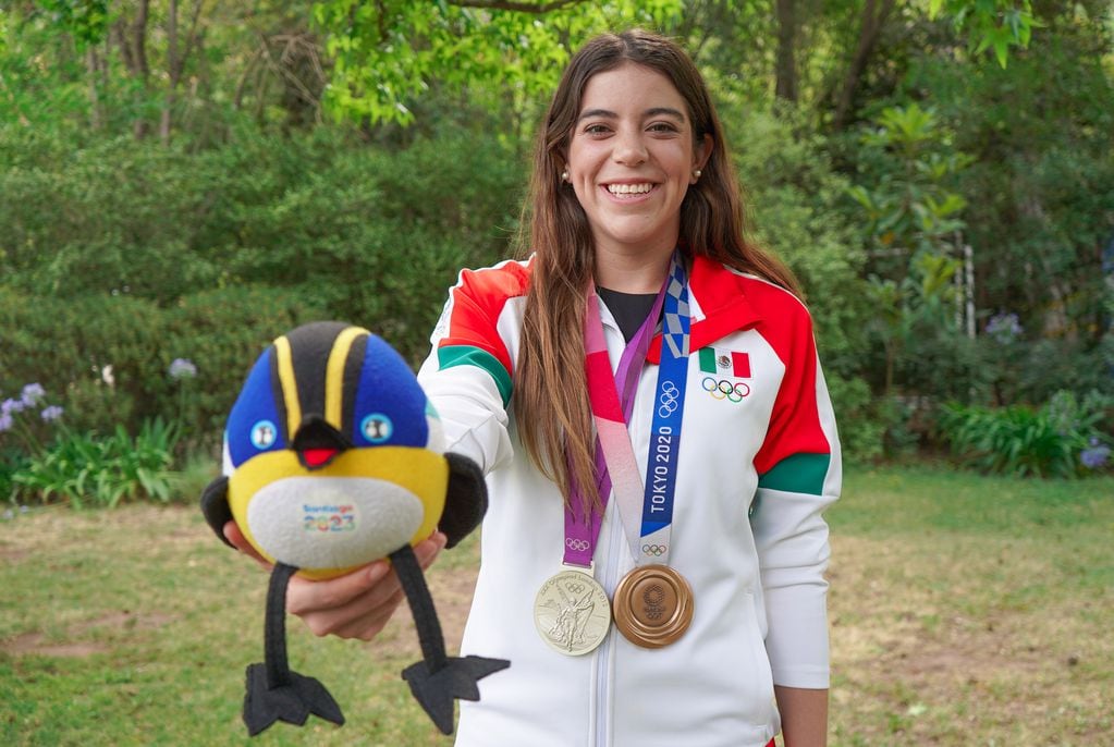 La clavadista mexicana Alejandra Orozco, posando con Fiu, la mascota oficial de Santiago 2023, y sus dos medallas olímpicas. Foto: Panam Sports.